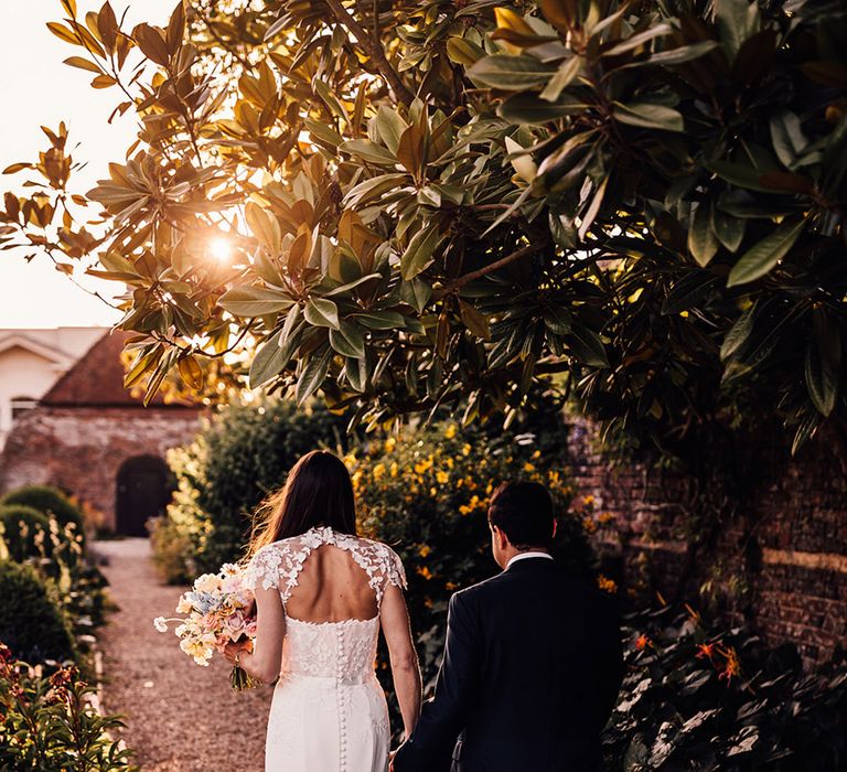 Bride in stunning lace sleeve wedding dress walking with the groom during golden hour 