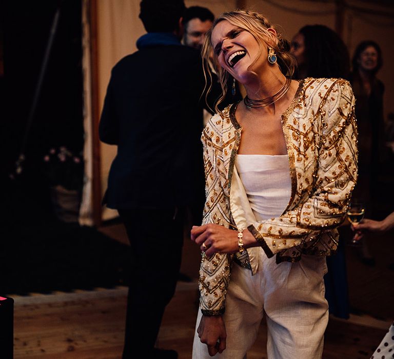 The bride in linen wedding trousers wearing a gold and white sparkly sequin beaded jacket 