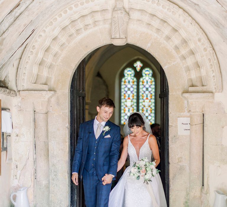 bride in an Made With Love wedding dress with bridal overskirt and groom in a check suit exiting the church wedding ceremony 