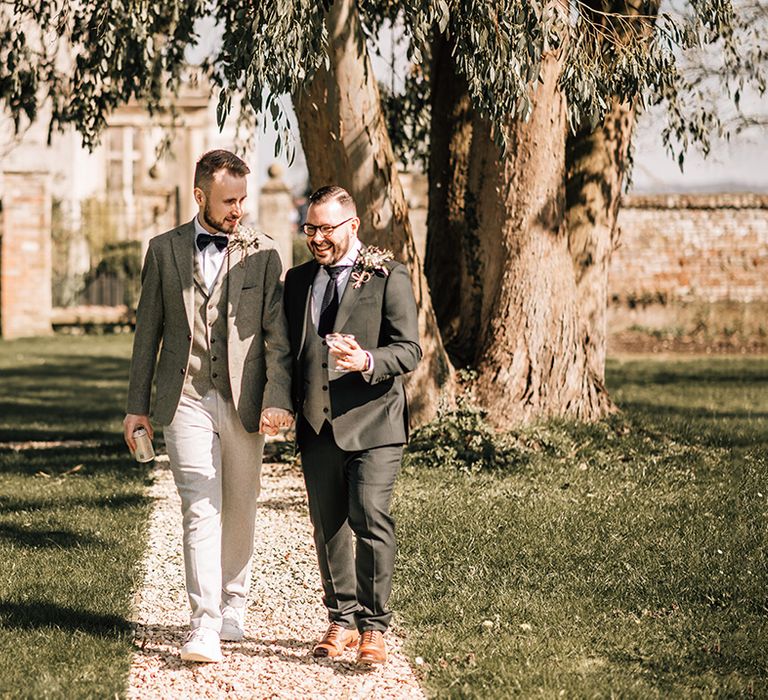 The grooms stroll around the country house wedding venue together in grey and black suits 