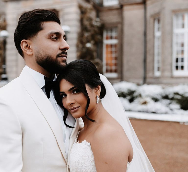 Groom in white tuxedo with the bride in a fitted lace wedding dress at winter wedding 