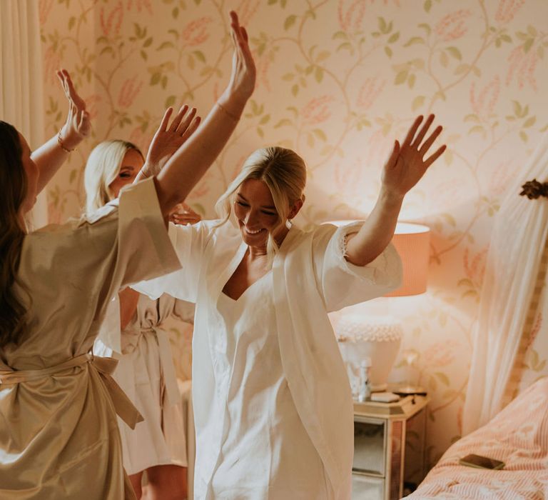 Bride in white pyjamas gets ready for the wedding dancing with bridesmaids