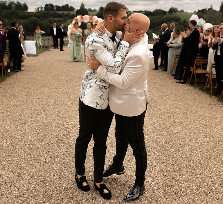 Two grooms share a kiss as they walk back down the aisle as a married couple at their outdoor ceremony 