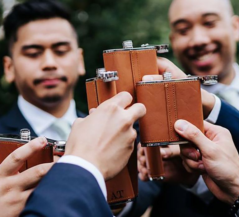 Grooms in dark blue suits toasting with brown leather hip flasks by Michael Maurer Photography