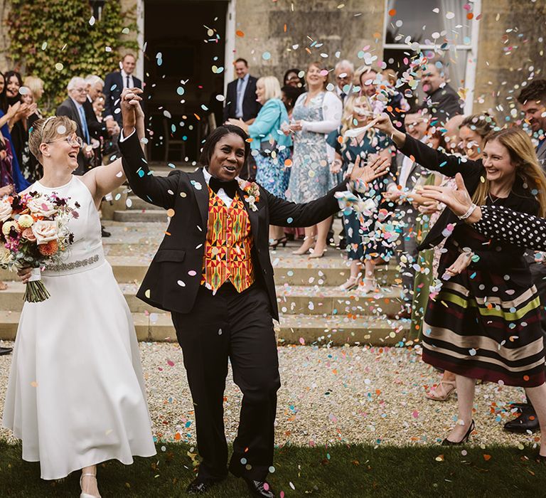 Two brides celebrate at the wedding as they exit to pastel wedding confetti 