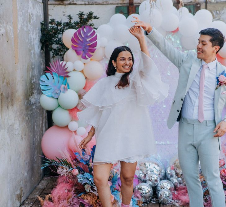 Bride and groom dancing in front of their sequin, glitter balls and balloon wedding altar 