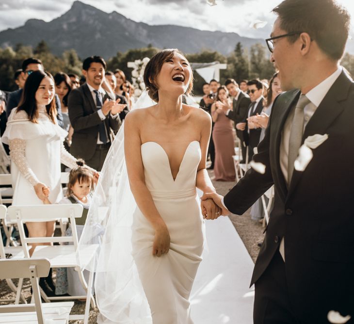 Bride in strapless Reem Acra wedding dress laughing down the aisle 