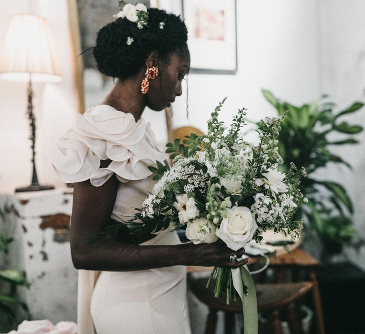 Hairstyles for Black brides. A Black bride wears tiny plaits in an updo. She wears a gold dress and holds her bouquet in her right hand.