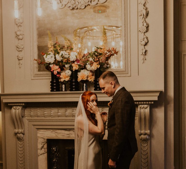 Bride and groom photography in Old Marylebone Town Hall, bride wears simple silk wedding dress and dries her tears whilst groom looks lovingly at his new bride 