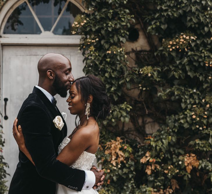 Black bearded groom in a velvet tuxedo kissing his brides forehead in a strapless Oleg Cassini wedding dress 