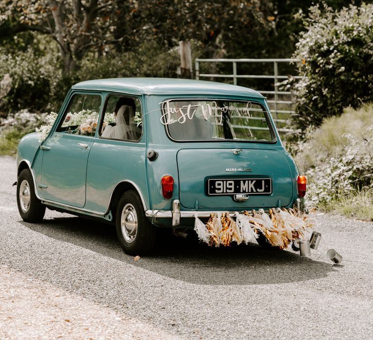 A small blue vintage mini drives off with a Just Married sign across the back window.