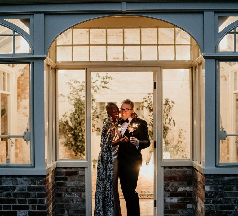 Bride and groom holding sparklers in the doorway at Our Beautiful Glasshouse in Sussex