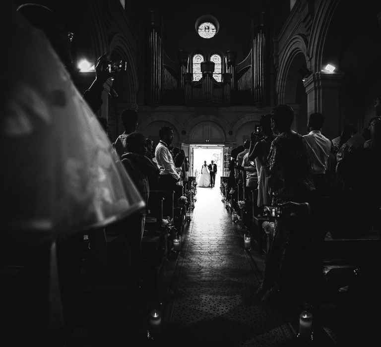 The bride beginning to enter the grand church at the bottom of the aisle