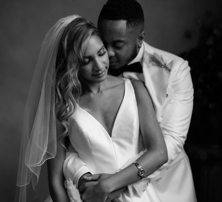 Intimate black and white wedding portrait of the groom embracing his bride by Paul and Nanda Photography 