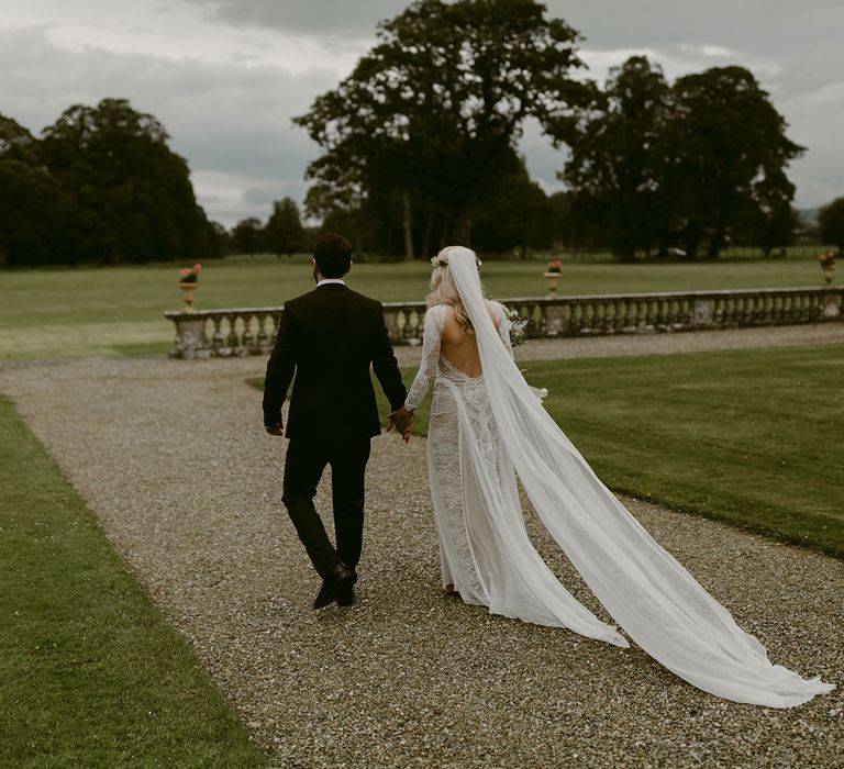 Bride in Grace Loves Lace wedding dress and single tier cathedral length veil walks with groom in black Hugo Boss suit at Drenagh Estate Wedding