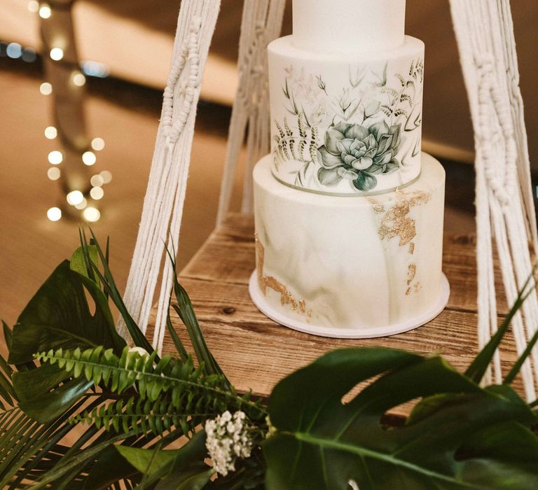 Cake is suspended on macrame with wooden board below 