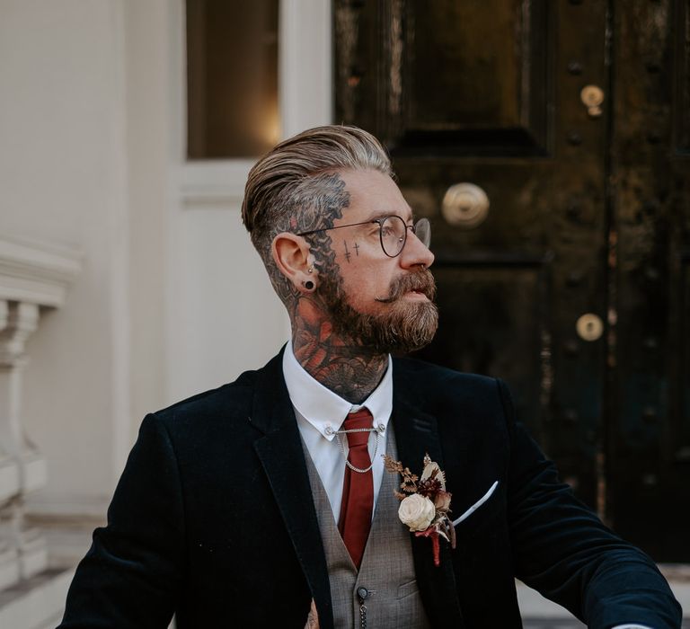 Side profile of white tattooed groom with slicked back hair and glasses in three piece suit