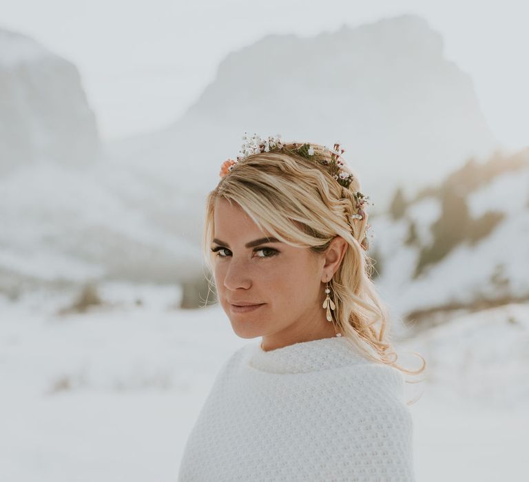 Beautiful bride with half up half down wavy hairstyle wearing a delicate flower crown and dangly earrings holding a autumn coloured wedding bouquet 