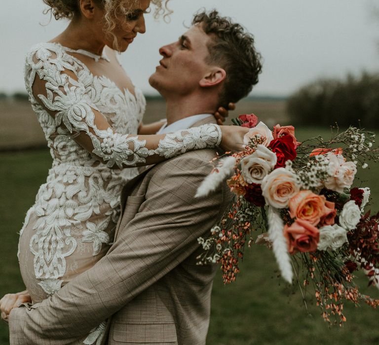 Bride being lifted up by groom in a field at Hornington Manor