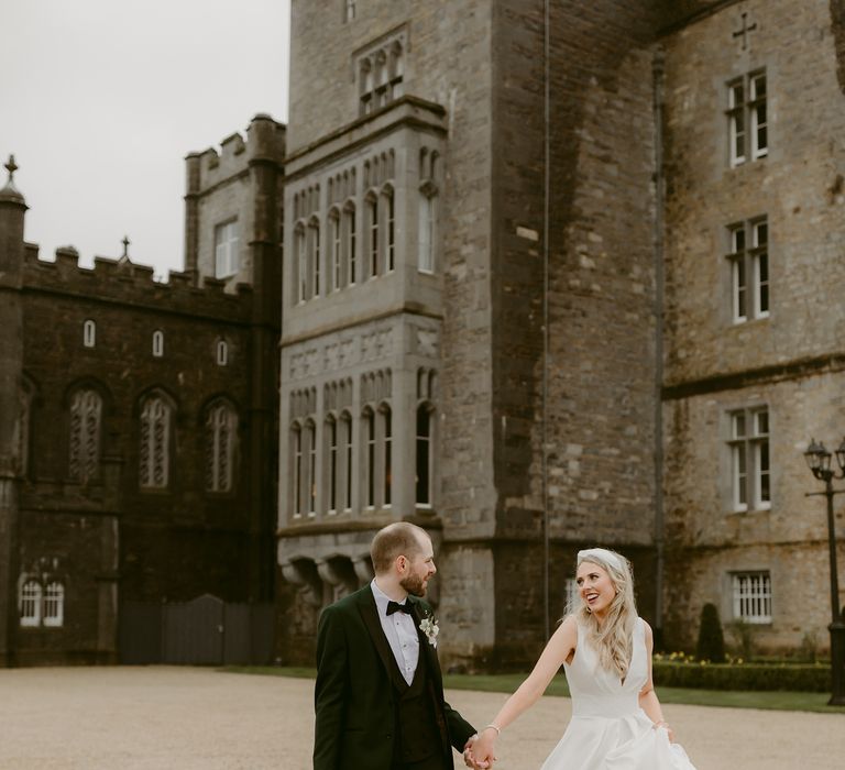 Bride & groom walk together hand in hand outside Markree Castle on their wedding day outdoors