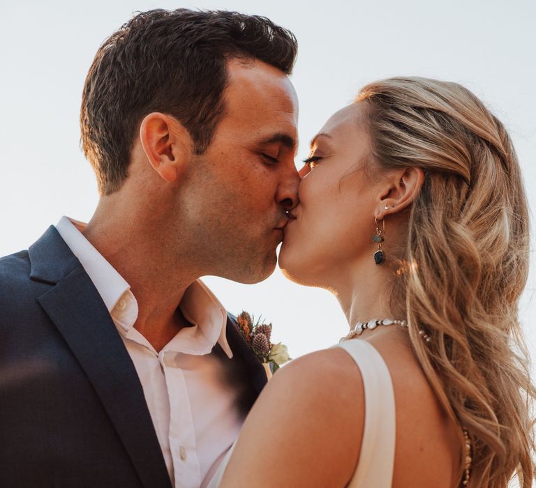 Bride & groom kiss as bride wears low cut back wedding gown