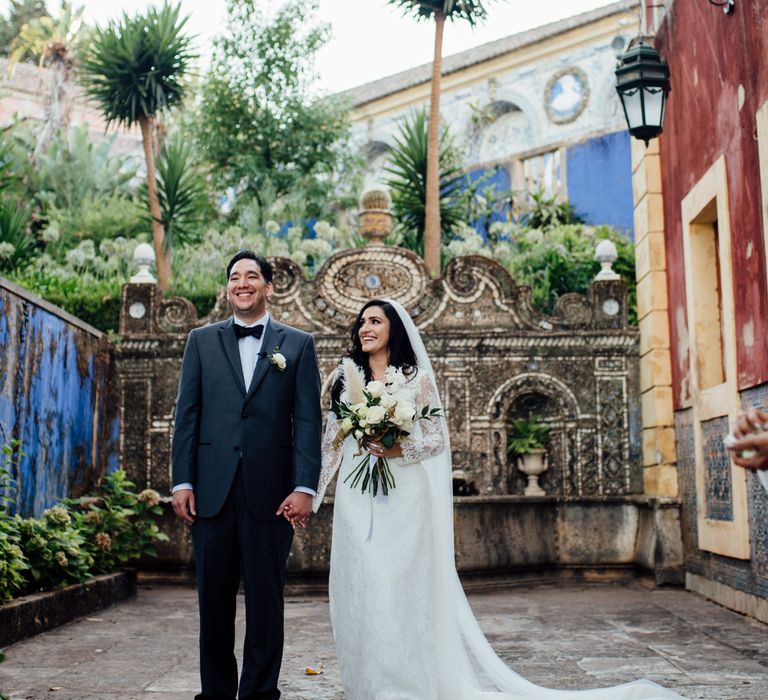 Bride & groom stand outdoors as bride holds classic white bouquet with pampas grass