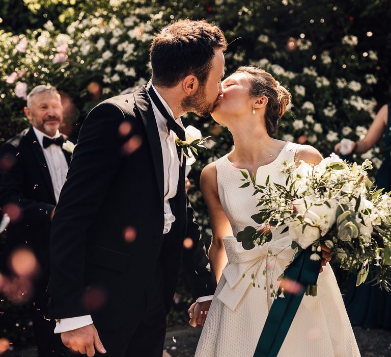 Bride & groom kiss outdoors as the sun shines around them