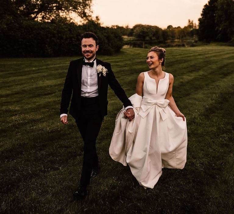 Bride & groom walk across manicured lawns on their wedding day