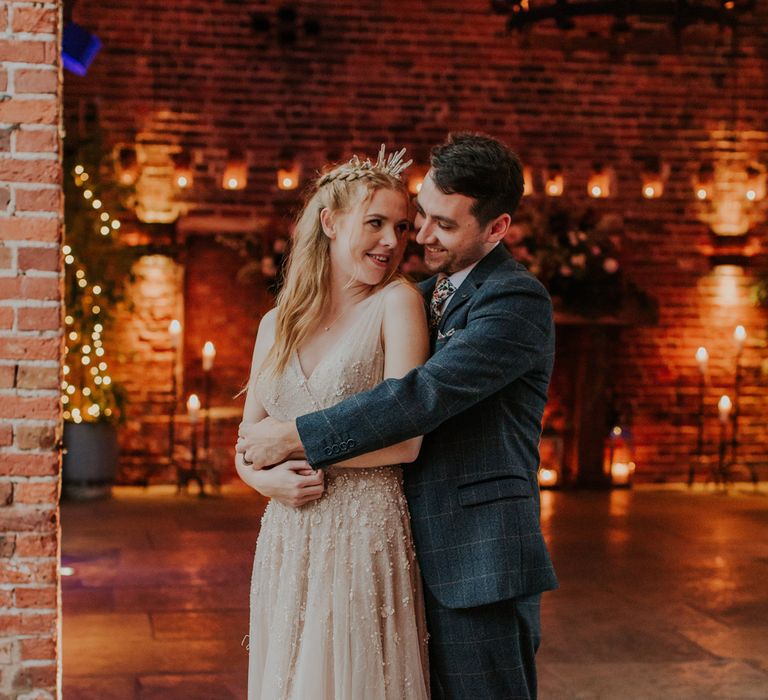 Groom in a check suit embracing his bride in a tulle wedding dress and bridal crown at their rustic barn wedding 