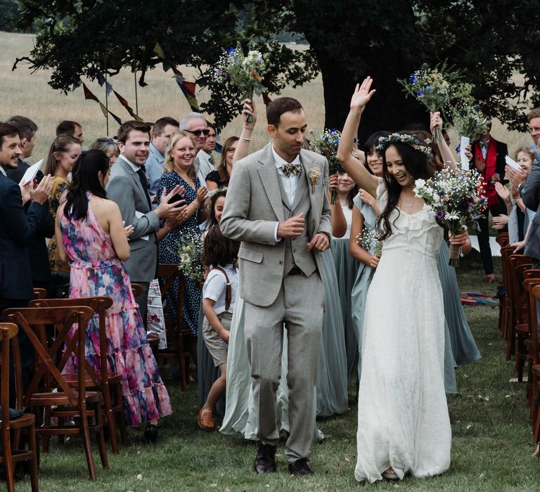 Bride celebrates as she walks down the aisle after wedding ceremony as wedding guests clap around them