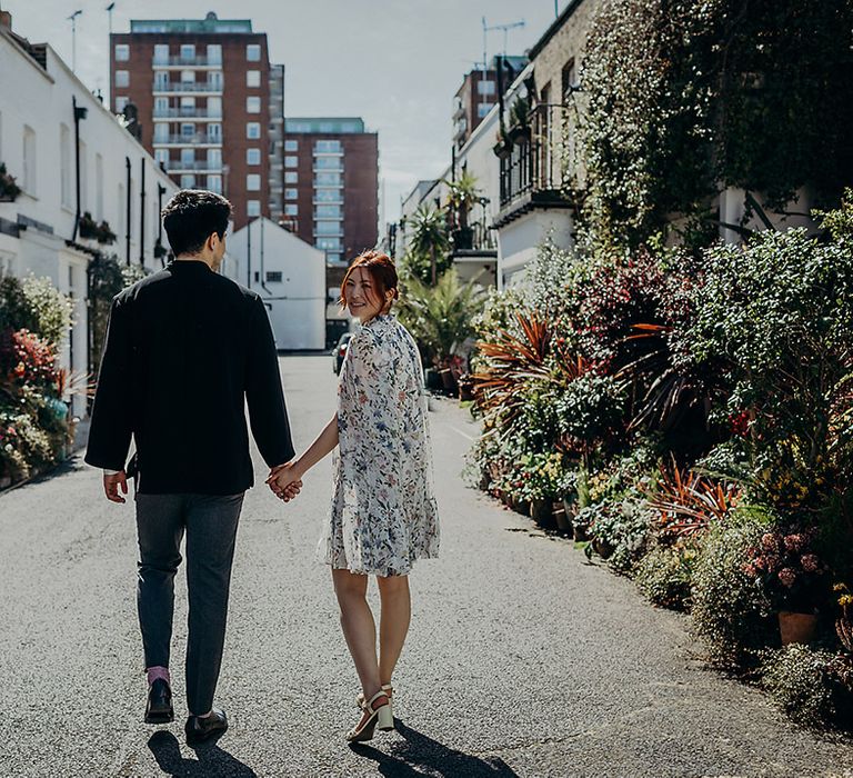 Bride in a short wedding dress with blue floral print and cape sleeves holding hands with her husband in Marylebone, London 