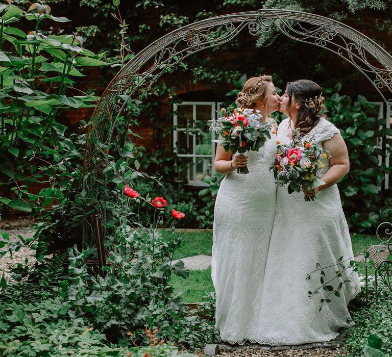 Brides kiss in gardens as they hold brightly coloured bouquets on the day of their wedding