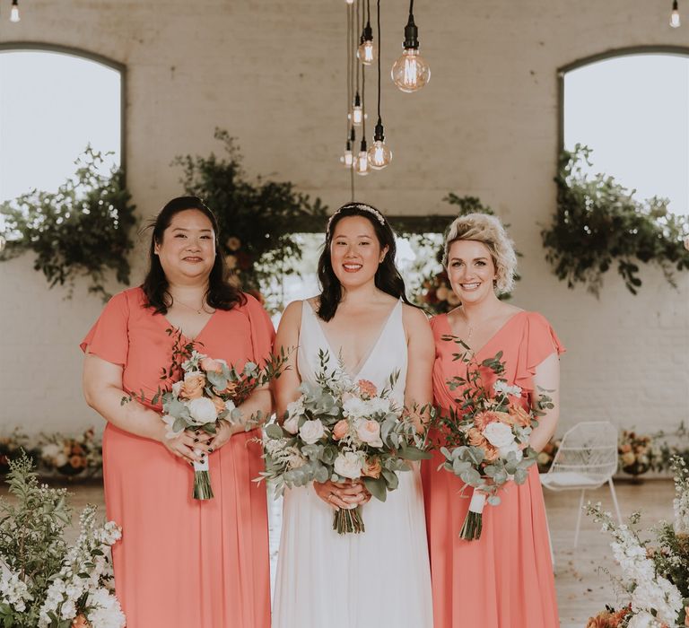 Bride and her bridesmaids in peach dresses holding bouquets with David Austin roses and eucalyptus at Osea Island Wedding 