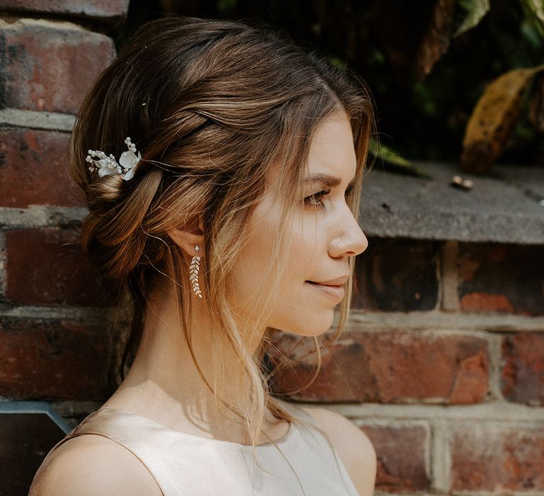 Bride with pinned up wedding hair wearing a flower hair pin, leaf earrings and champagne gold Constellation Ame bridesmaid dress