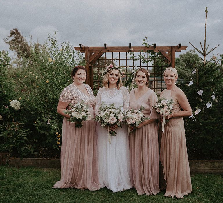 Bridal party portrait at back garden wedding with pregnant bride in a long sleeve wedding dress and flower crown and bridesmaids in pink chiffon dresses 