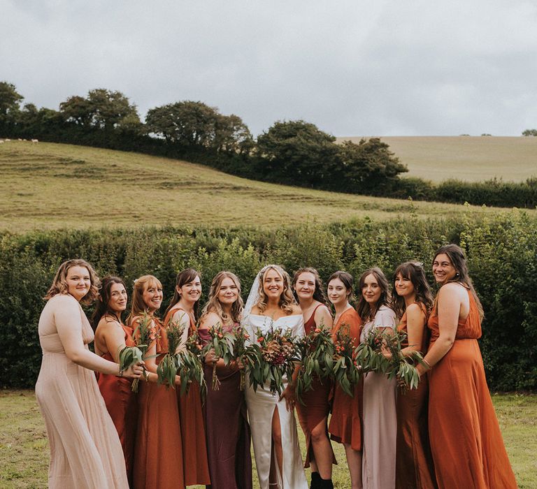 Bride stands with her bridesmaids who wear differing styles of bridesmaids gowns 