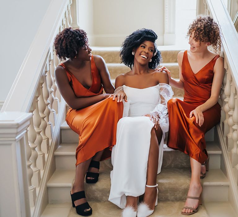 Bridal party portrait on the stairs at Modern Hall with bride in a strapless wedding dress and pom pom shoes, and bridesmaids in orange satin dresses 