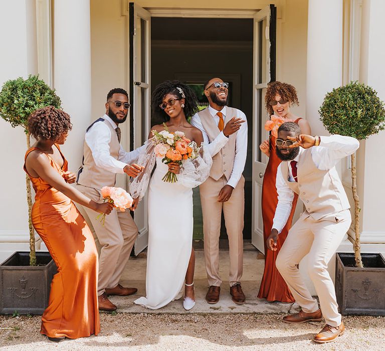 Wedding party picture with bride in a strapless wedding dress, bridesmaids in orange satin dresses and groomsmen beige suits