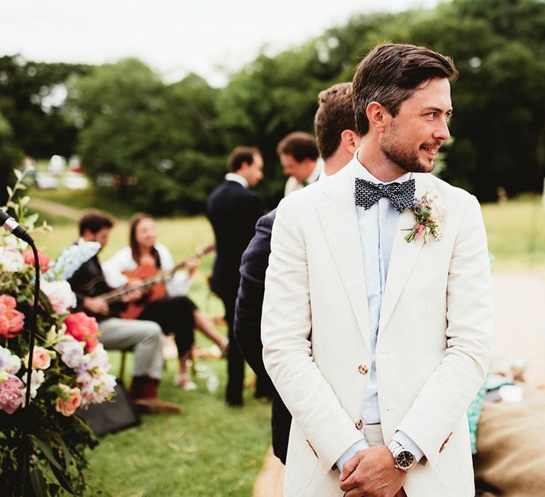 Groom awaits his bride whilst wearing light coloured blazer and blue bow tie