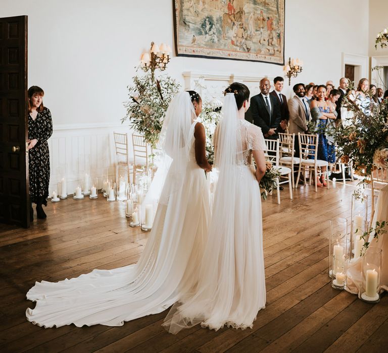 Two brides walking down the aisle together at their same-sex Elmore Court wedding ceremony 