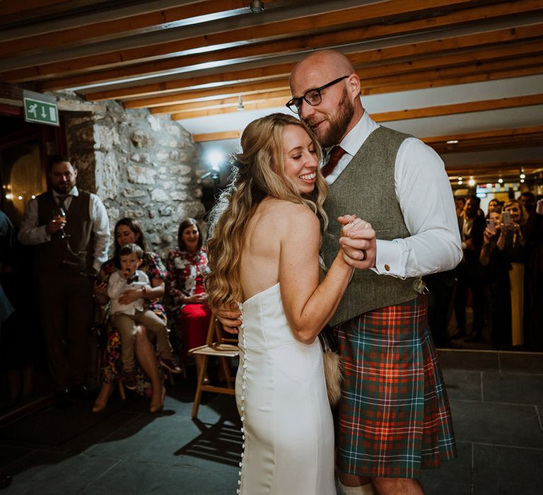 Bride & groom embrace during reception as groom wears vegan sporran 