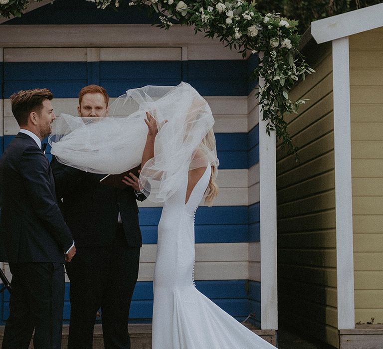 Brides veil blows in the wind at coastal wedding