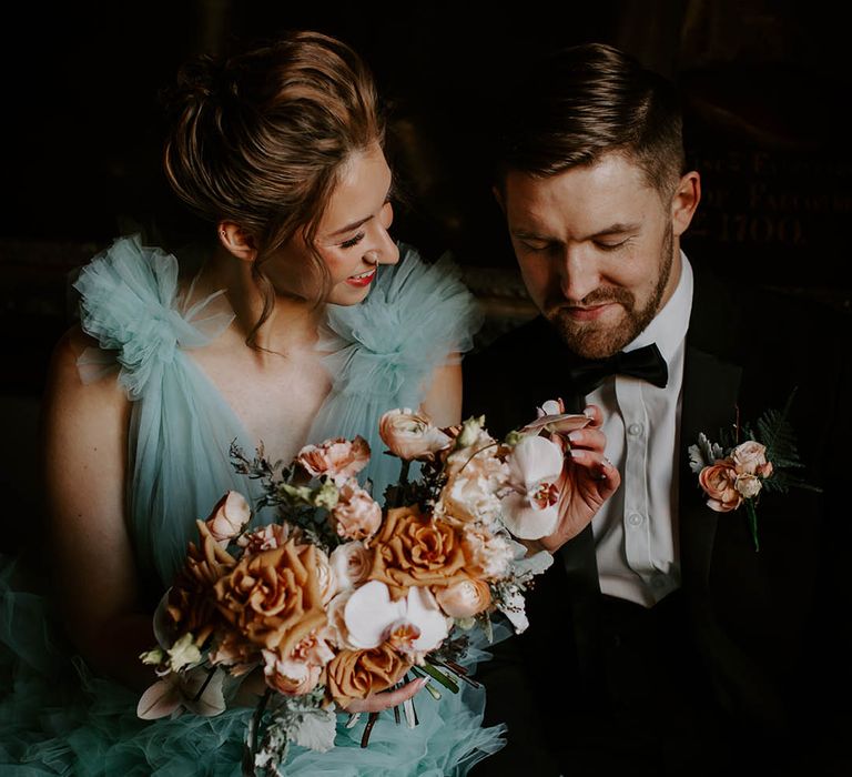 Bride in a blue wedding dress holding a peach and cafe au late wedding dress with roses, orchids and ranunculus flowers 