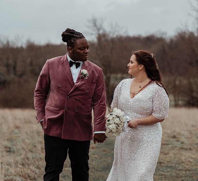 Bride & groom stand on fields on their wedding day whilst looking lovingly at one another