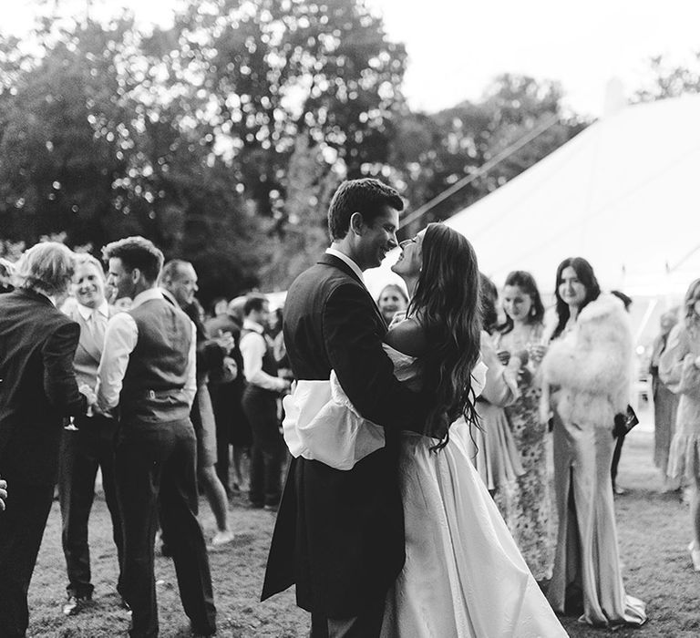 Bride and groom share a private moment in front of their mingling wedding guests at marquee wedding 