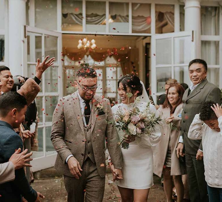 Newlyweds walking through pink confetti with neutral floral bouquet 