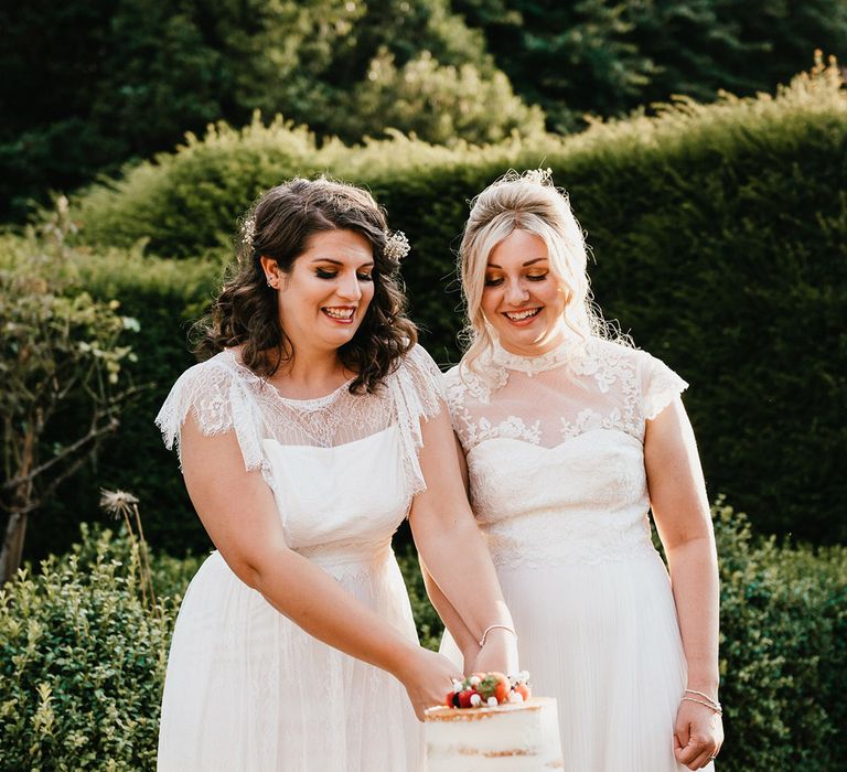 Brides cut their two-tier semi-naked white frosted wedding cake together with summer berries and gypsophila decor