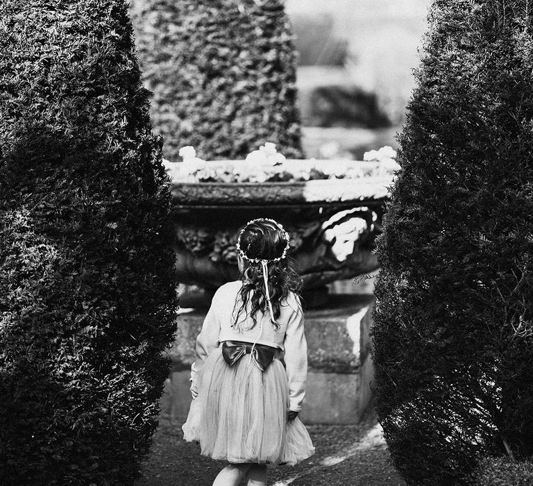 Flower girl with flower crown and tulle dress looks around the gardens of the wedding venue |