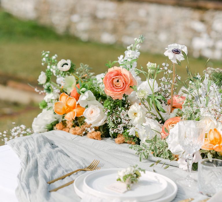 outdoor wedding tablescape with flower table runner and white place settings with gold cutlery 