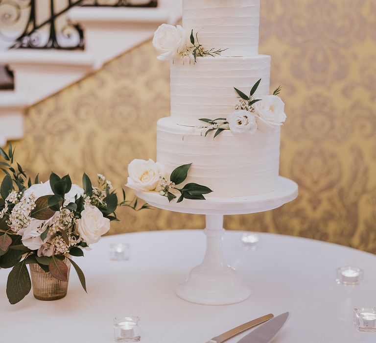 Three tier white frosted wedding cake with white roses and foliage 